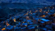 Vista aérea al anochecer de un barrio en ladera con casas apiladas y ventanas iluminadas